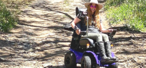 Leonie sitting in her Magic Mobility Extreme X8 Power Chair, easily navigating the rugged outdoor terrain